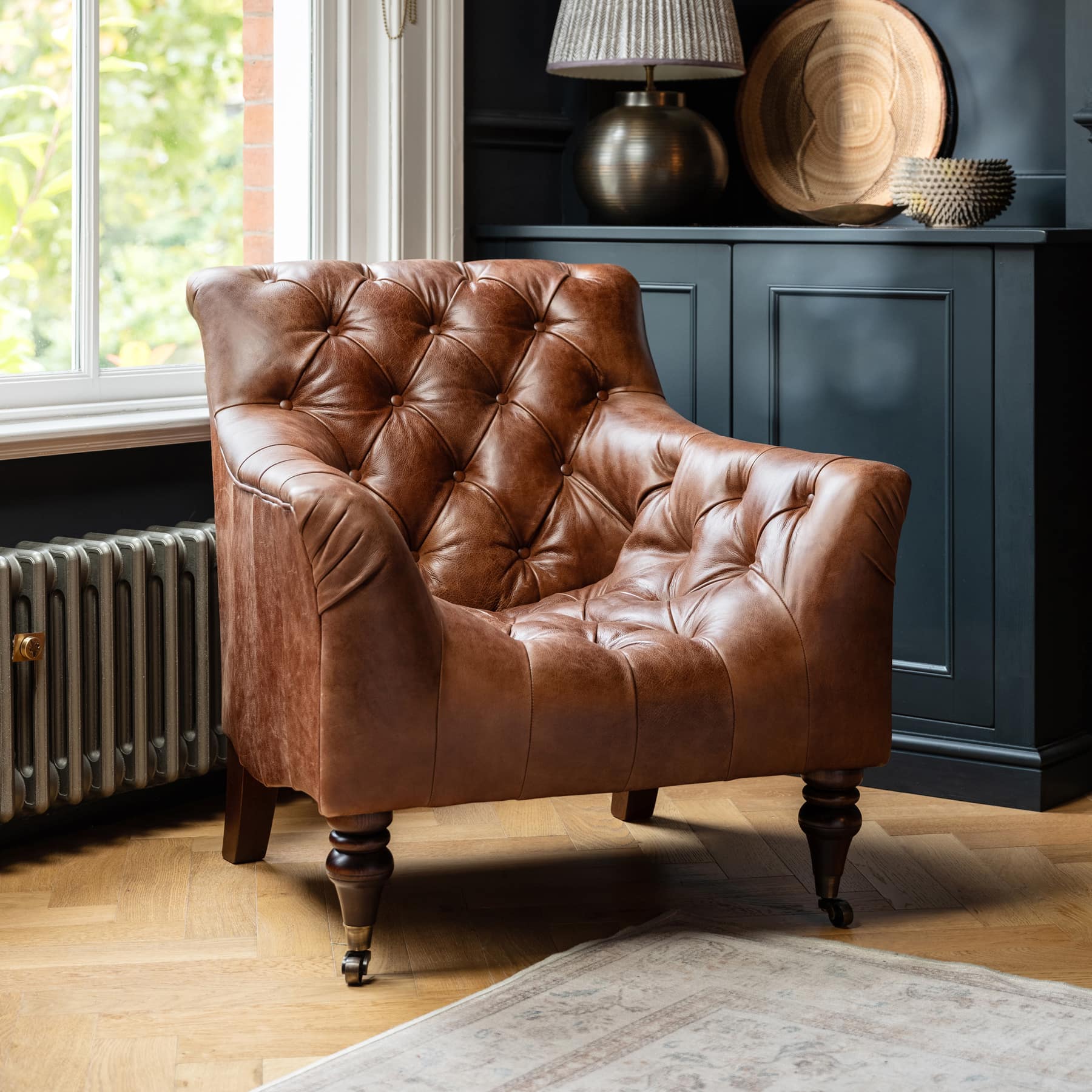 Tetrad Yale Sessel in cognacfarbenem Leder mit tiefen Knöpfen im eleganten Wohnzimmer vor Fenster und dunklem Sideboard